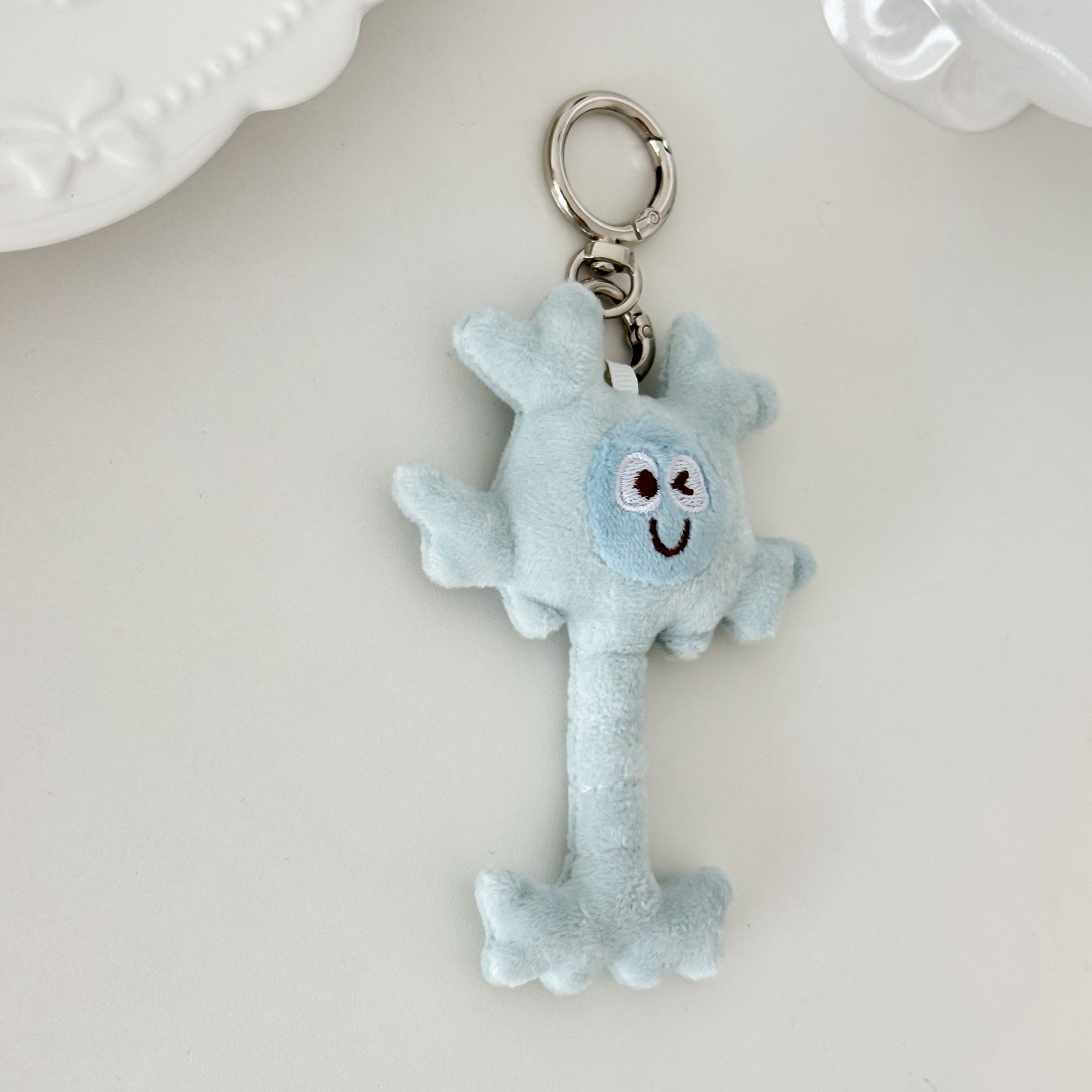 Light blue neuron plush keychain with embroidered facial features and lightweight design.