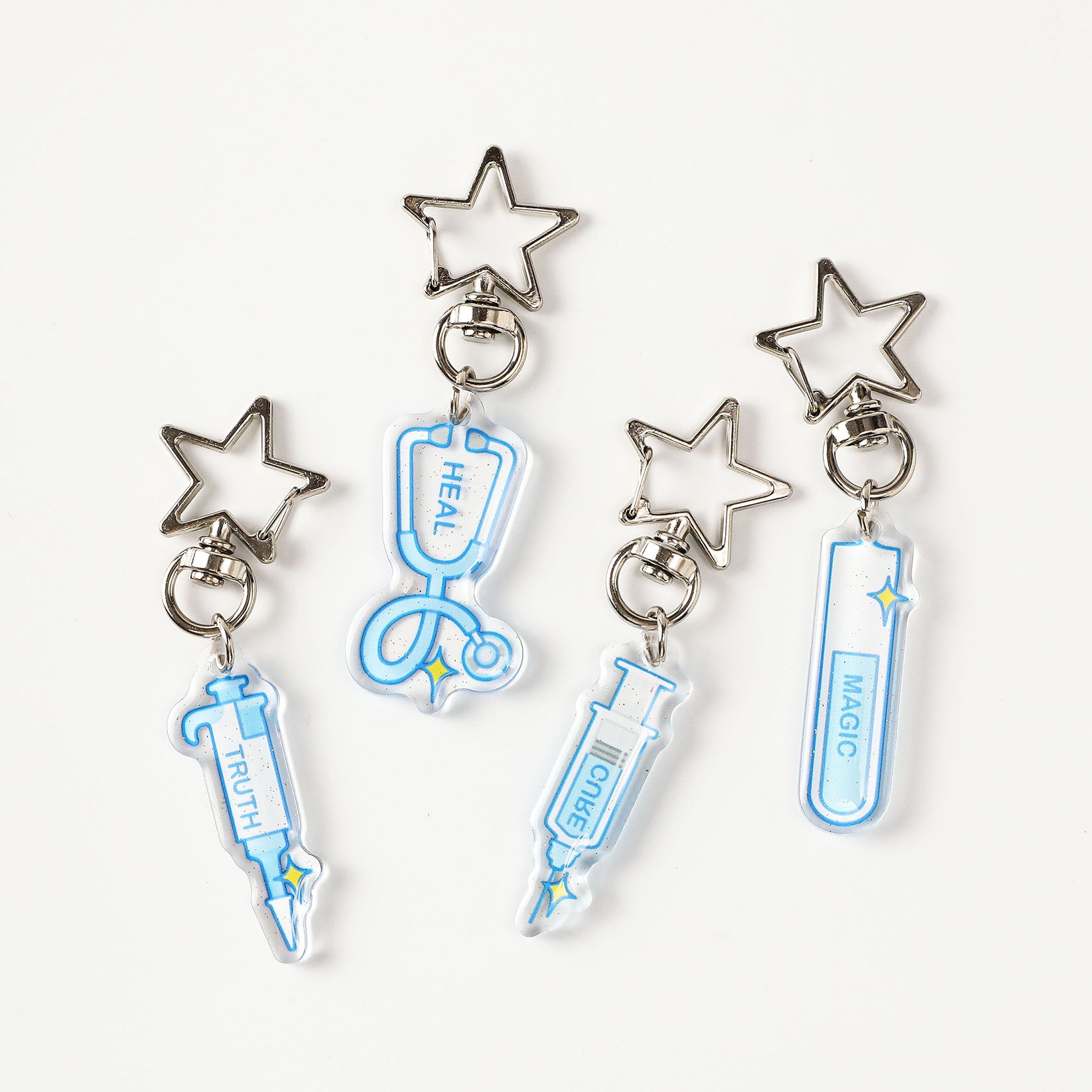 Blue science acrylic keychain set featuring pipette, stethoscope, test tube, and syringe designs with glitter finish and star-shaped metal clasps.