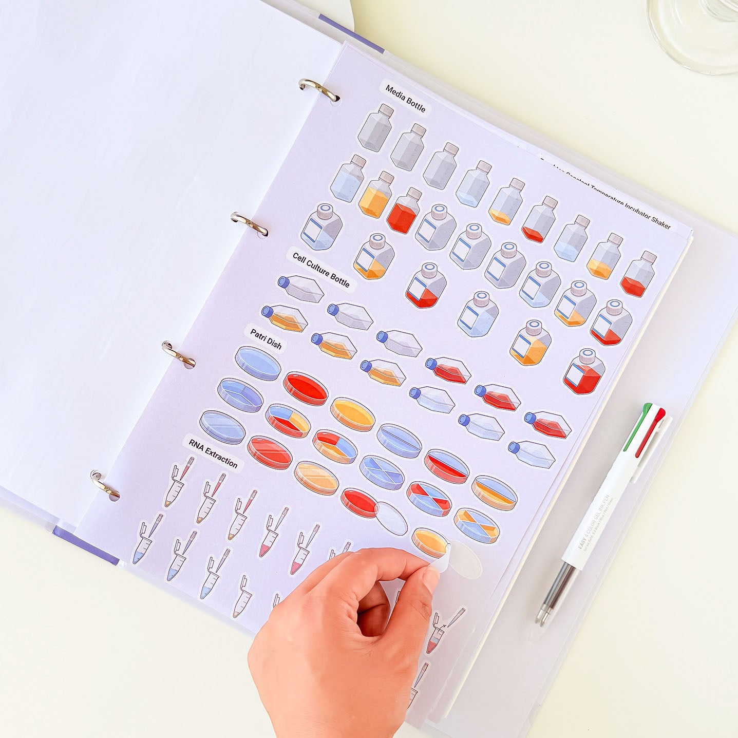 Laboratory notebook with illustrated pages featuring culture bottles, Petri dishes, microcentrifuge tubes, and cell culture equipment.